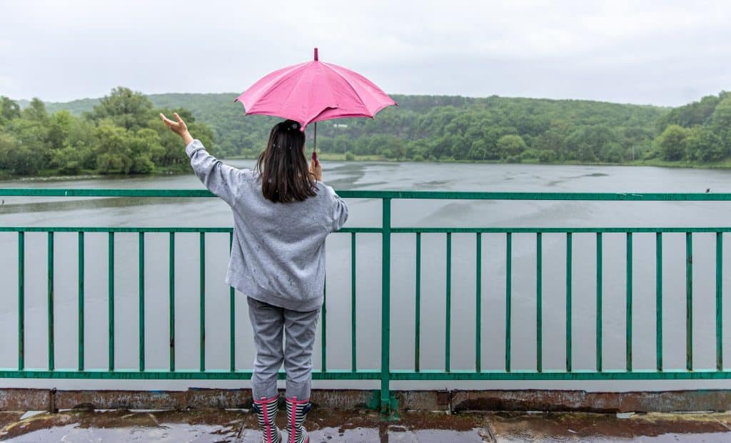 Person holding a pink umbrella in the rain beside a green metal railing