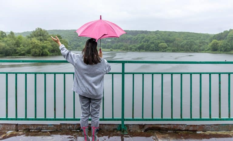 Person holding a pink umbrella in the rain beside a green metal railing